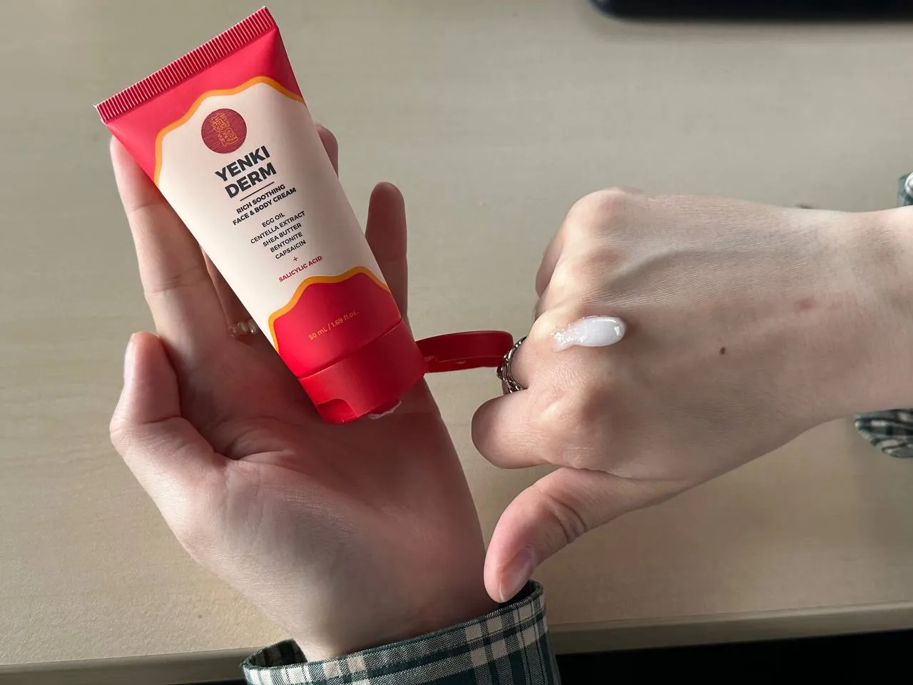 Manos sujetando el tubo de Yenki Derm con una porción de crema blanca en el dorso